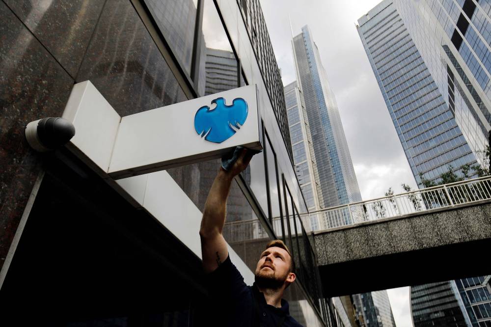 رجل ينظف لافتة خارج فرع بنك باركليز في مدينة لندن. 